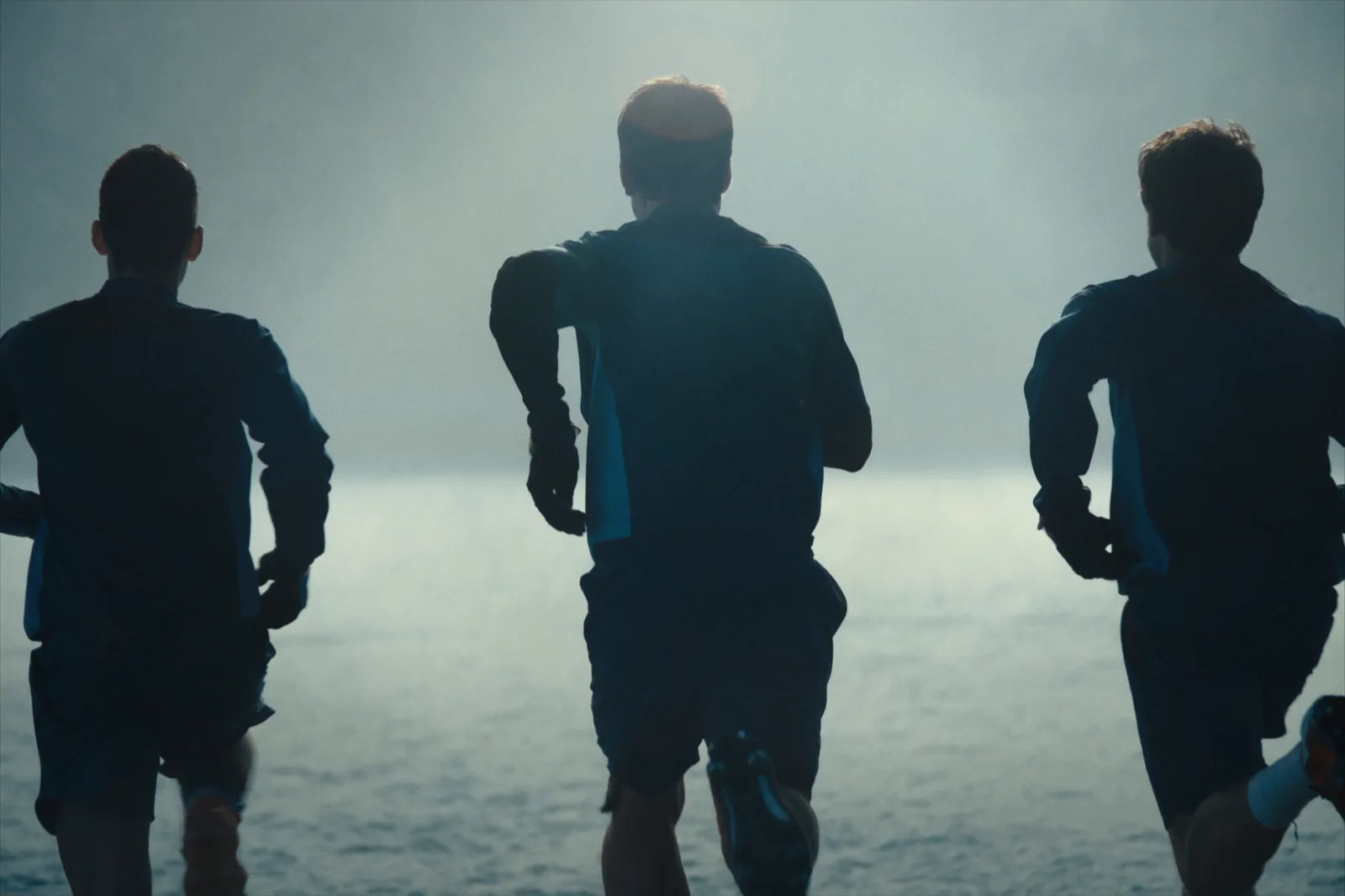 Three players sprinting across a foggy training pitch in winter.
