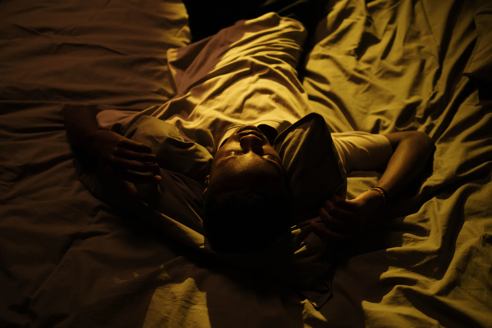 A man lies in a warmly lit bed at night.