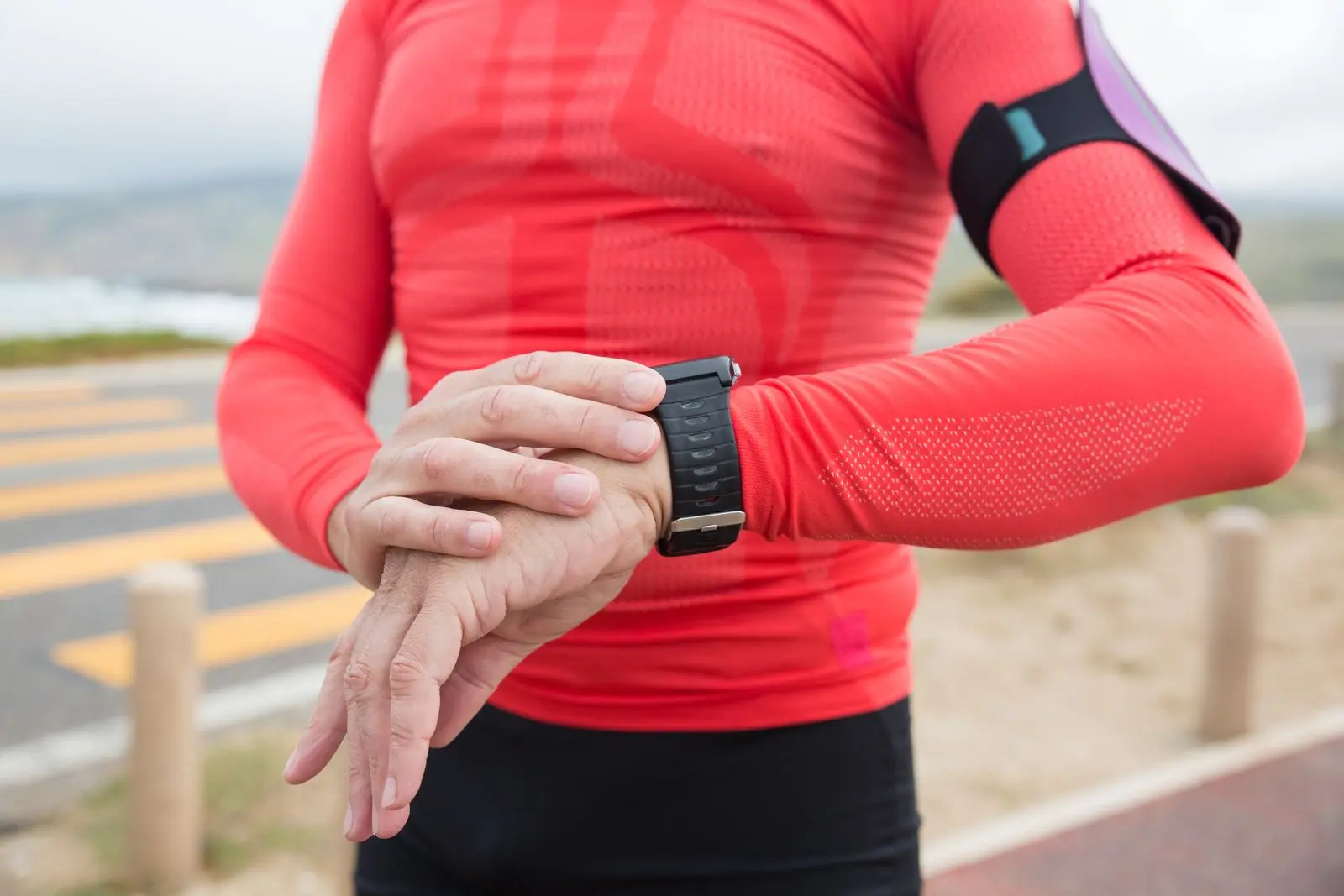 Runner in a red shirt checking the sports watch on his wrist.