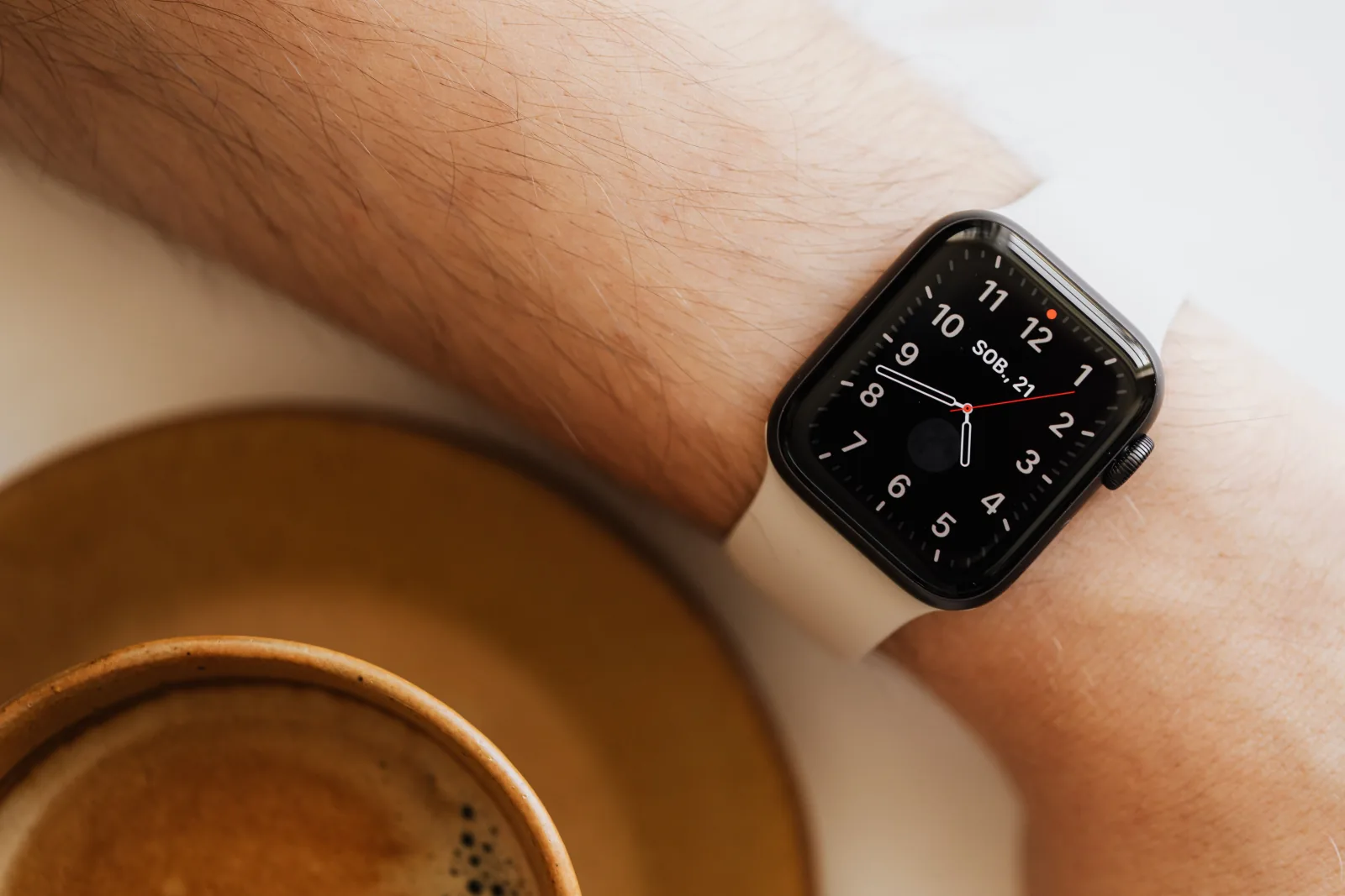 Close-up of a smartwatch on a wrist beside a morning cup of coffee.