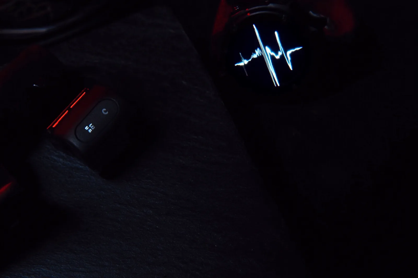 Heart rate chest strap and sports watch showing a pulse curve on a dark surface.