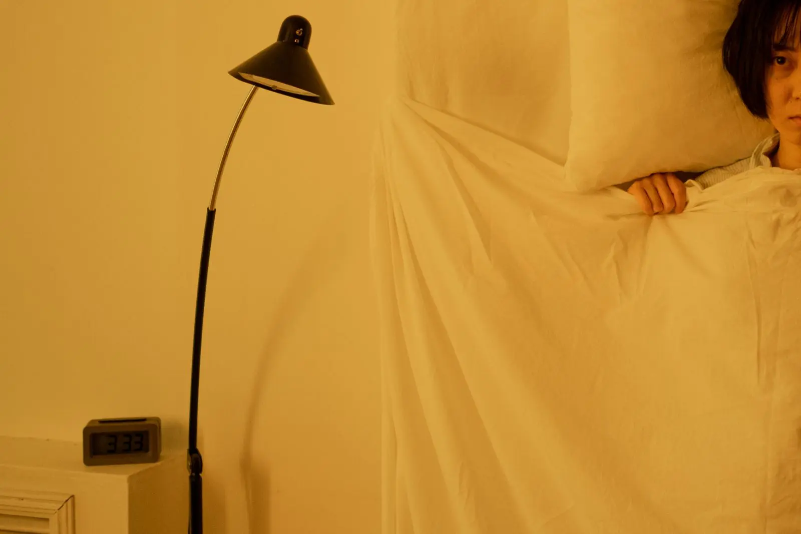 A person lies awake in bed at night, the clock beside them showing 3:33.
