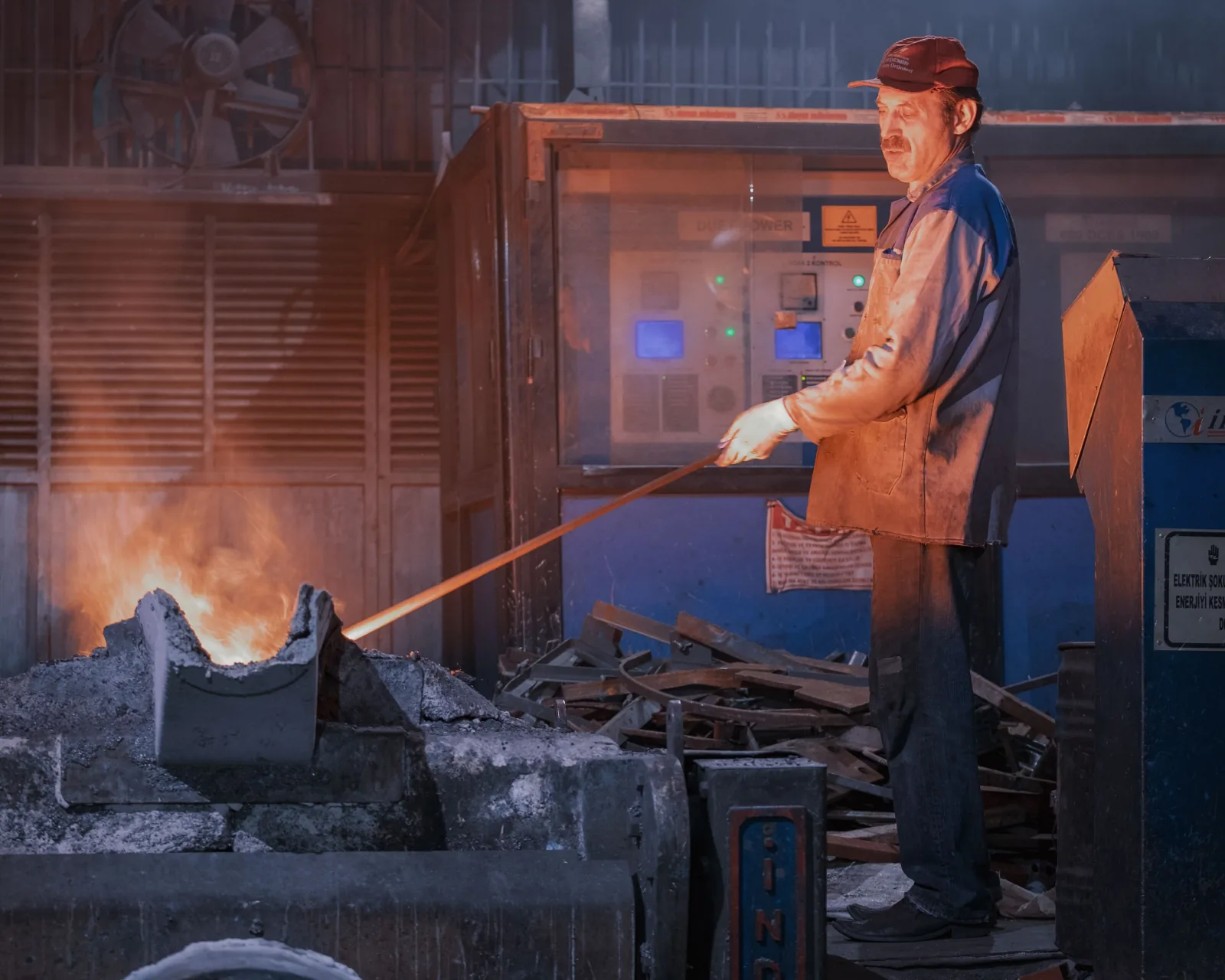 An industrial worker operates a furnace in a factory at night.