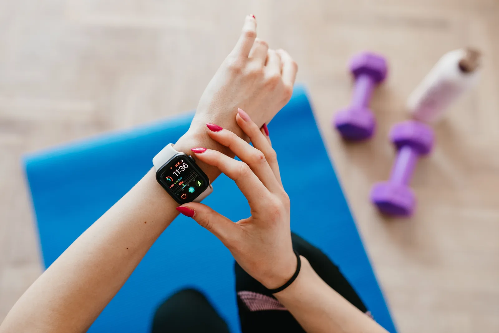 An athlete checks her smartwatch before training beside a mat and dumbbells.
