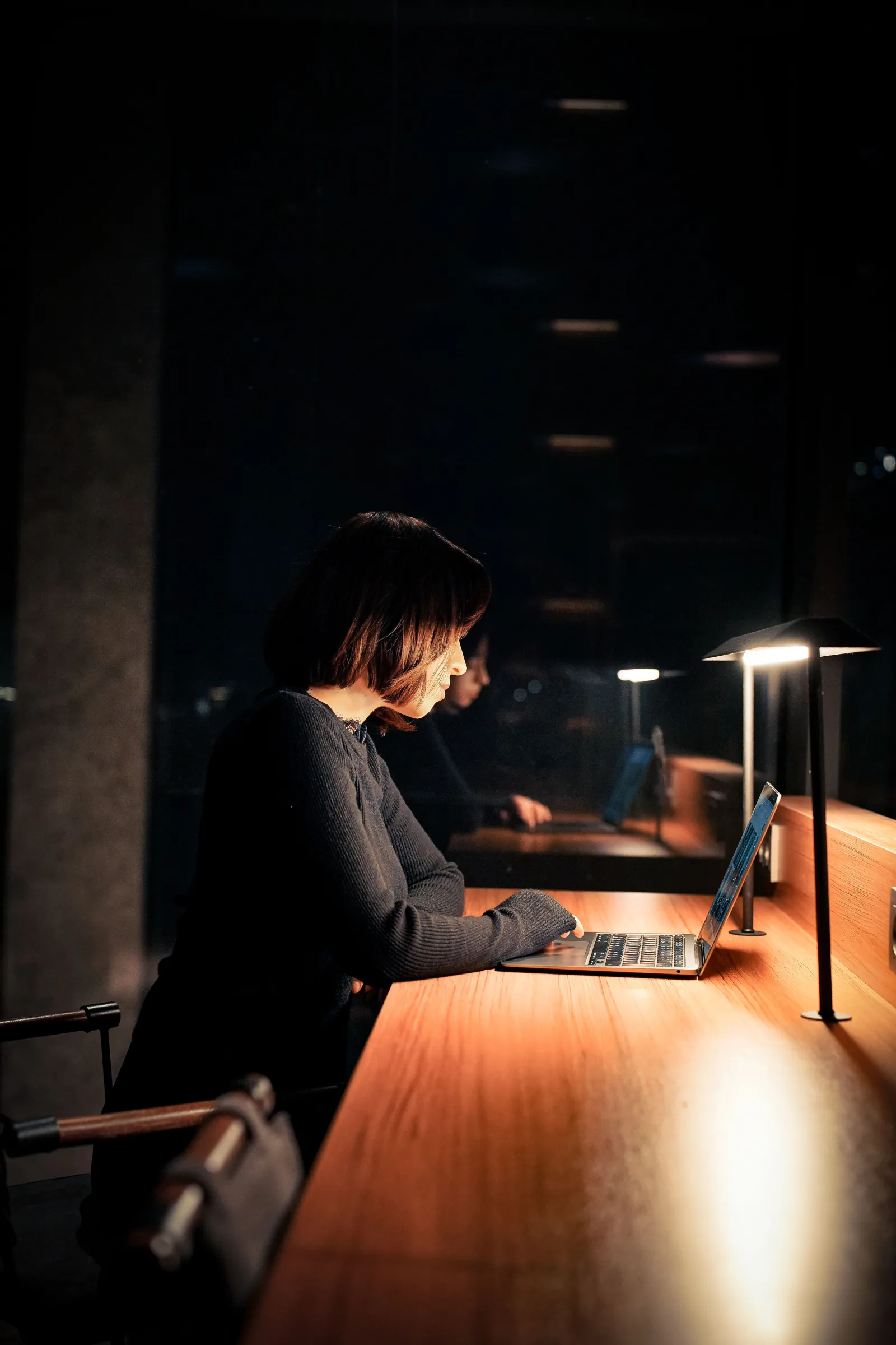 A woman works on a laptop at night in a dark reading room.