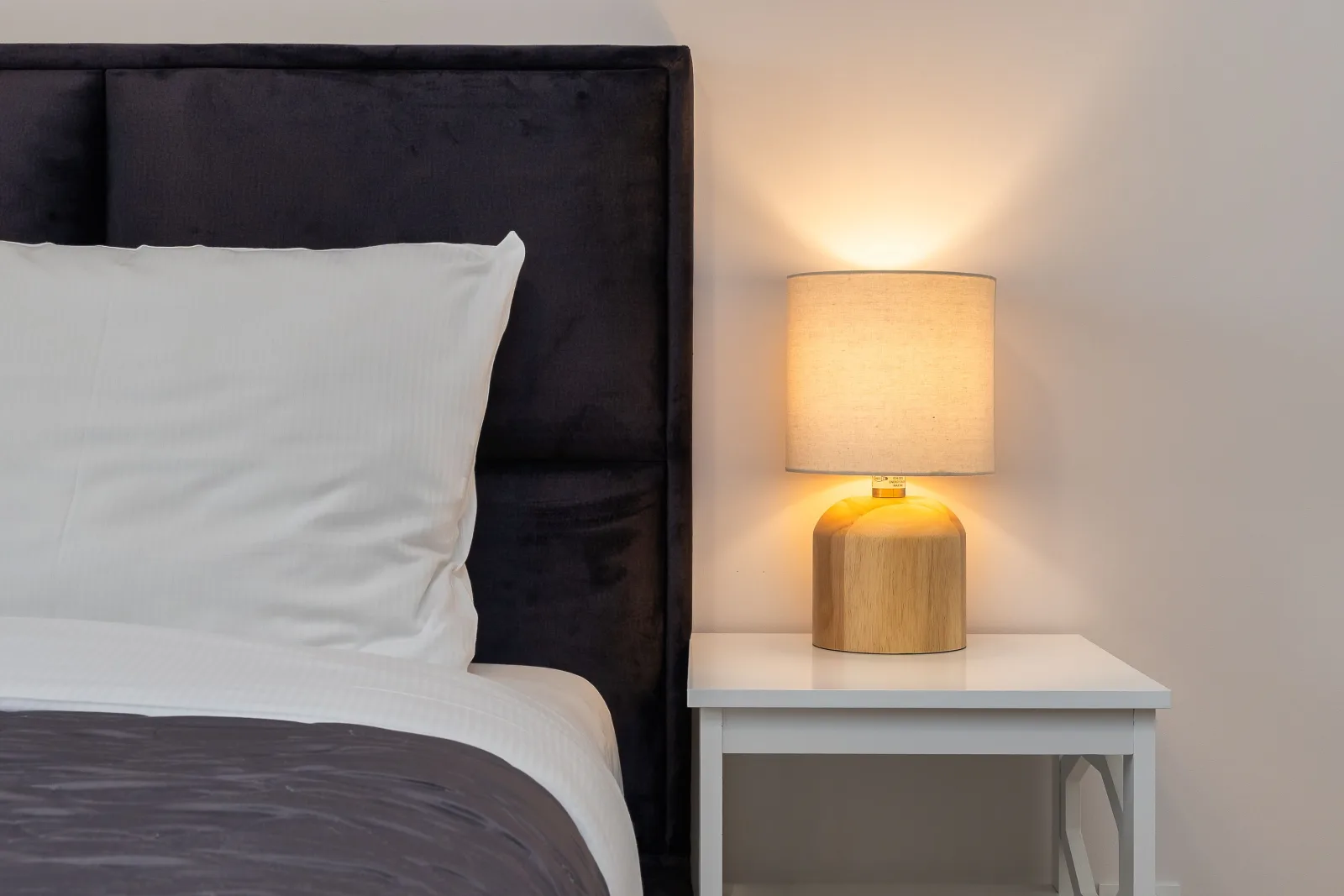A quiet bedroom with a made bed and a warm bedside lamp.