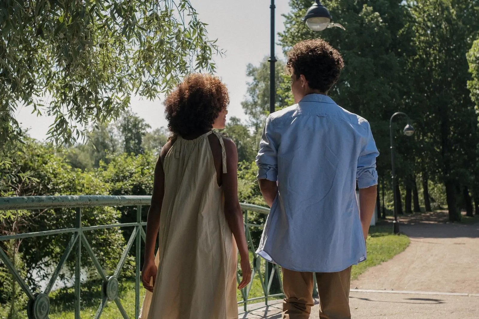 Two people walking together across a park bridge in summer.