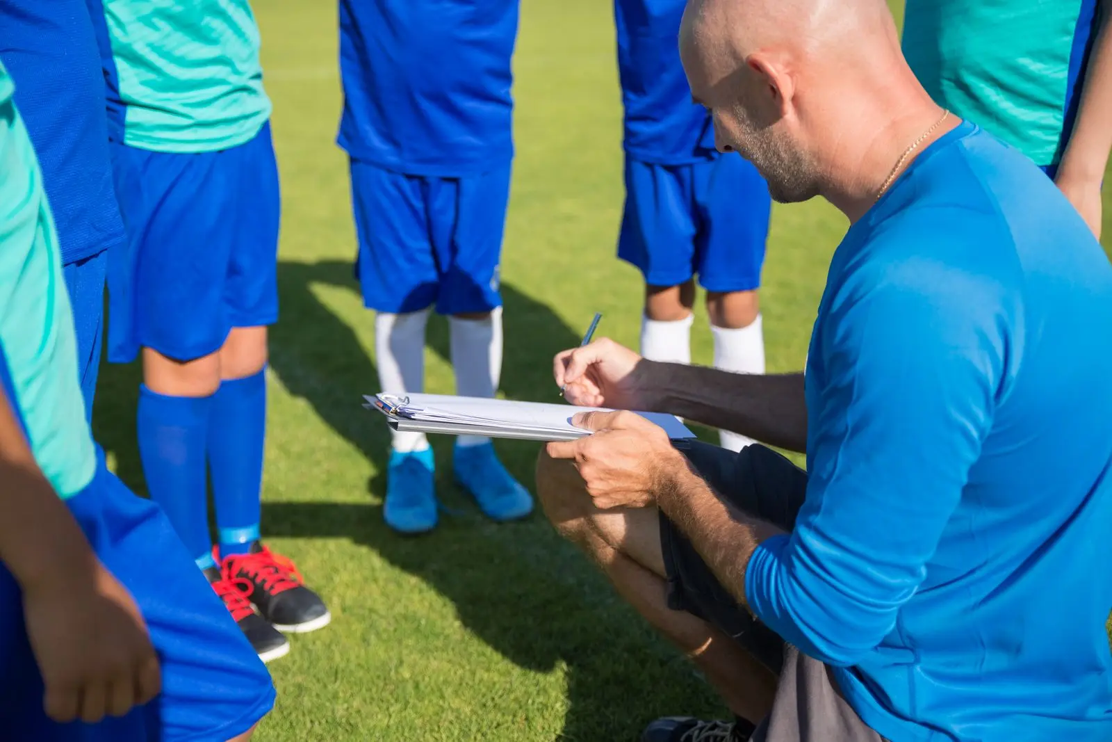 Youth coach taking notes on a clipboard in front of his team.
