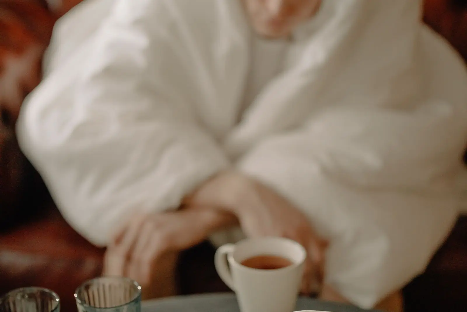 A person wrapped in a blanket sits in front of a cup of tea.
