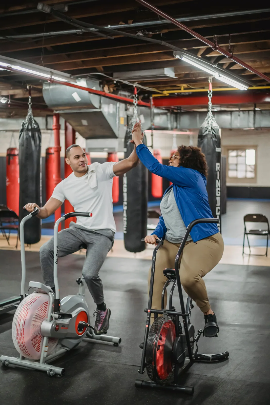 Trainer and athlete share a motivating high-five on air bikes in the gym.