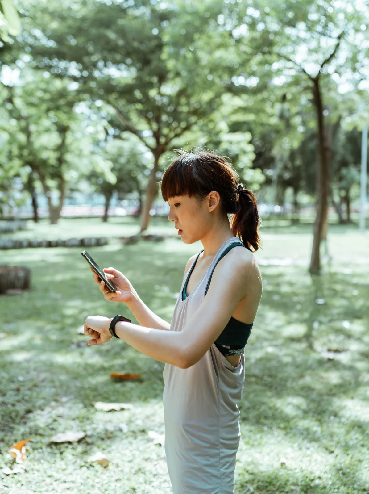 Athlete checks her smartwatch and smartphone in a quiet park.