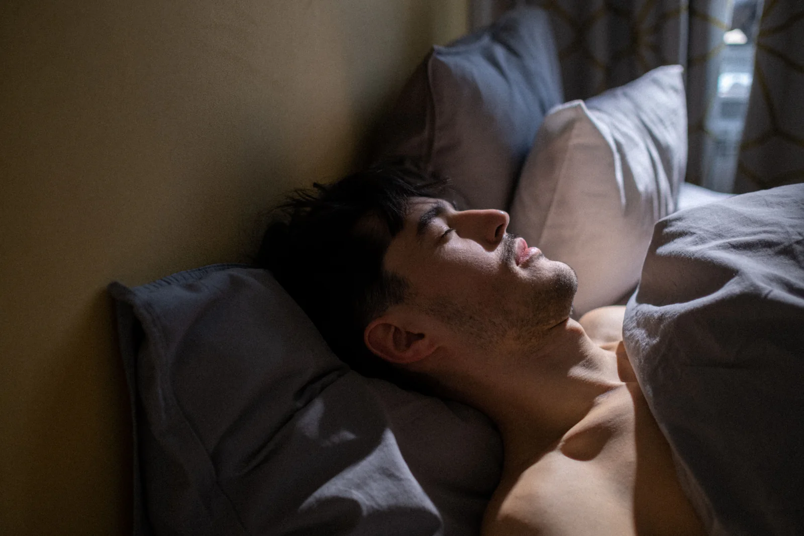 A man sleeps in a darkened bedroom.