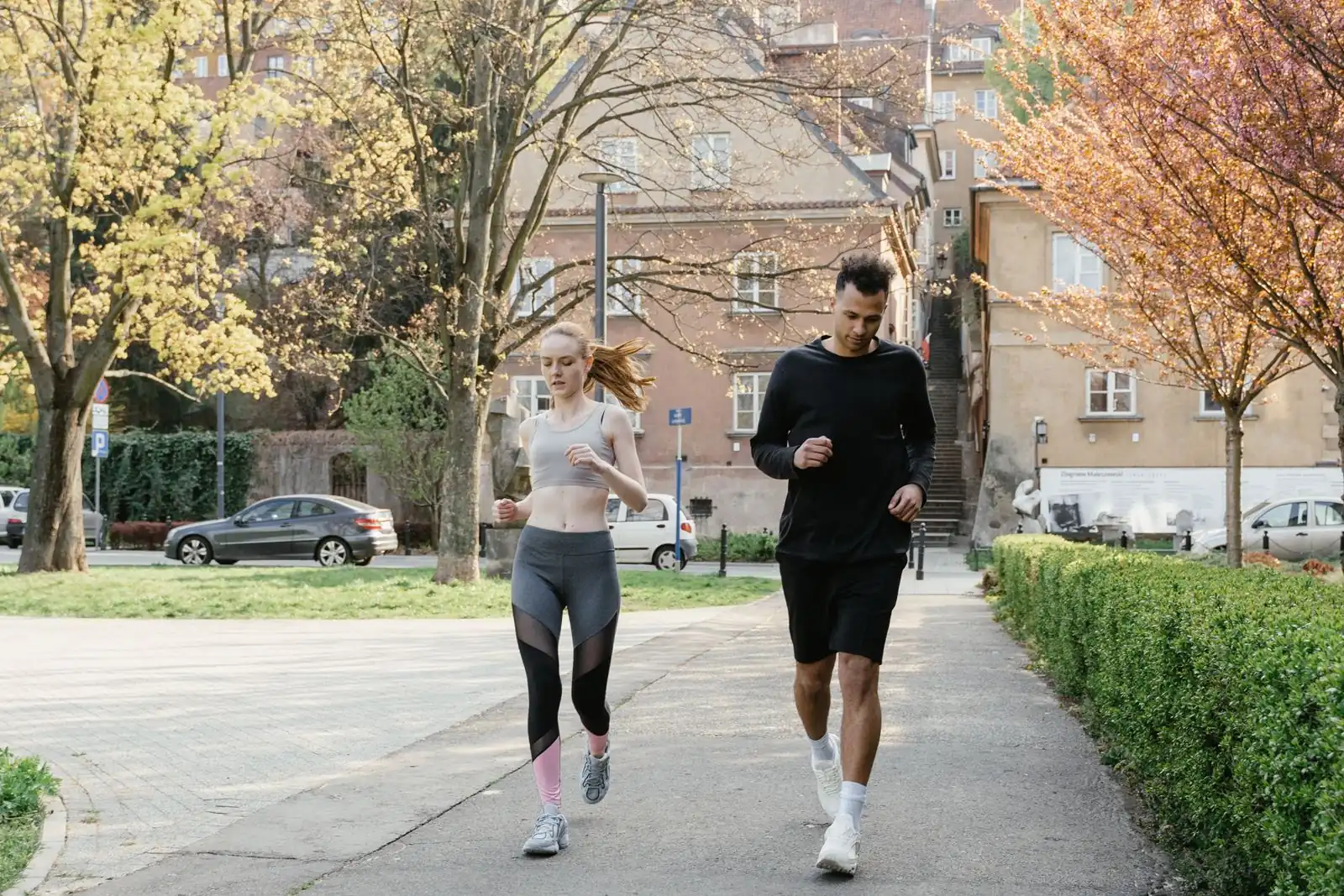 A woman and a man jog together on a path between blossoming trees.