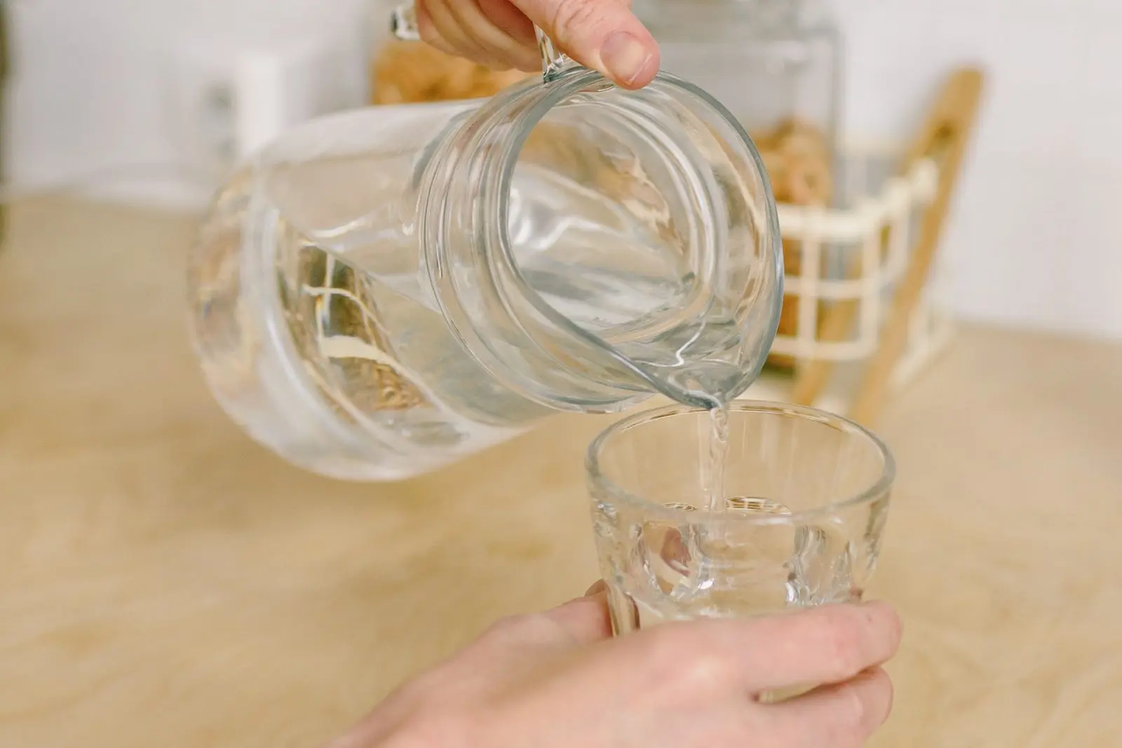 A glass of water being poured from a carafe.